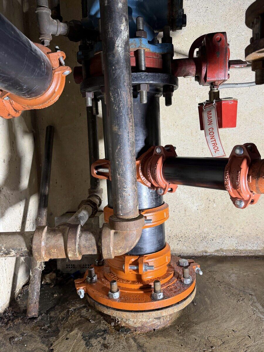 Newly fabricated flange, pipe, and fittings in a commercial fire-sprinkler riser room after Paragon's repair — clean joints and properly supported runs