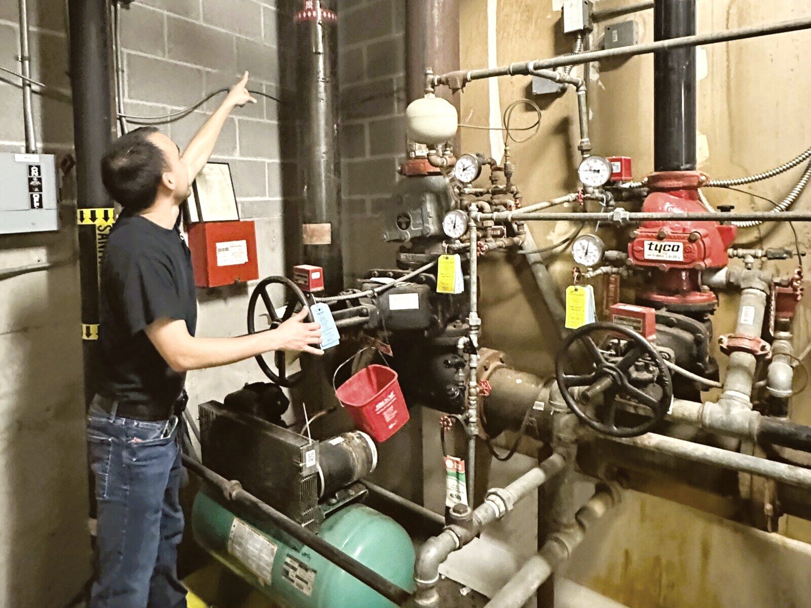 Paragon technician inspecting a commercial fire sprinkler riser, checking the dry-pipe valve, gauges, and air compressor