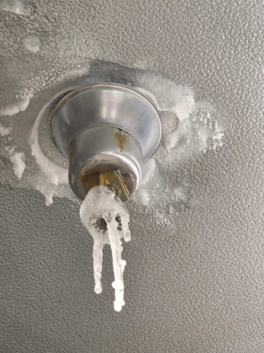 Leaking dry pendent sprinkler with ice built up around the head and icicles hanging below it