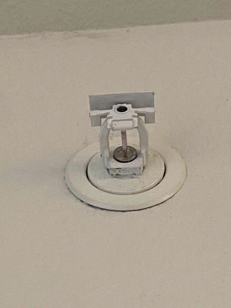Before: Sprinkler head — fully painted over by a previous building paint job → new listed head, mandatory replacement per NFPA 25.